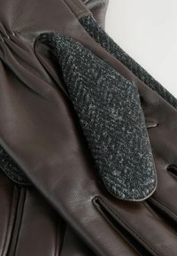 Pruunikas nahast kindad, millel on must villane detail randmeosas, mis näitab pehmet tekstuuri ja detailset õmblemist.