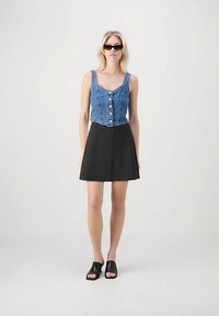 Top scurt din denim cu detalii cu nasturi, asortat cu o fustă evazată neagră cu buline și sandale negre fără baretă. Material neted, design conținut.