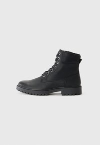 Botas de tobillo negras con cordones, hechas de cuero con un acabado texturizado, ojales de metal y una suela resistente. Forro suave en el cuello.
