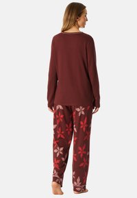 Conjunto de pijama color burdeos que incluye una parte superior de manga larga y pantalones con un estampado floral en rojo y rosa claro sobre un fondo oscuro. Ajuste suave y holgado.