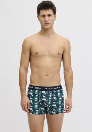 Young man standing, wearing dark boxer briefs with pink flamingo and green leaf print, and "JACK & JONES" waistband, neutral background.