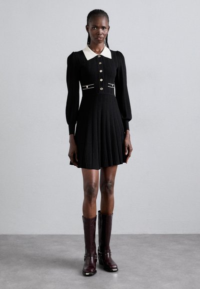 Vestido negro con plisado y un cuello blanco, con botones dorados y detalles plateados. Combinado con botas burdeos hasta la rodilla. Textura suave.