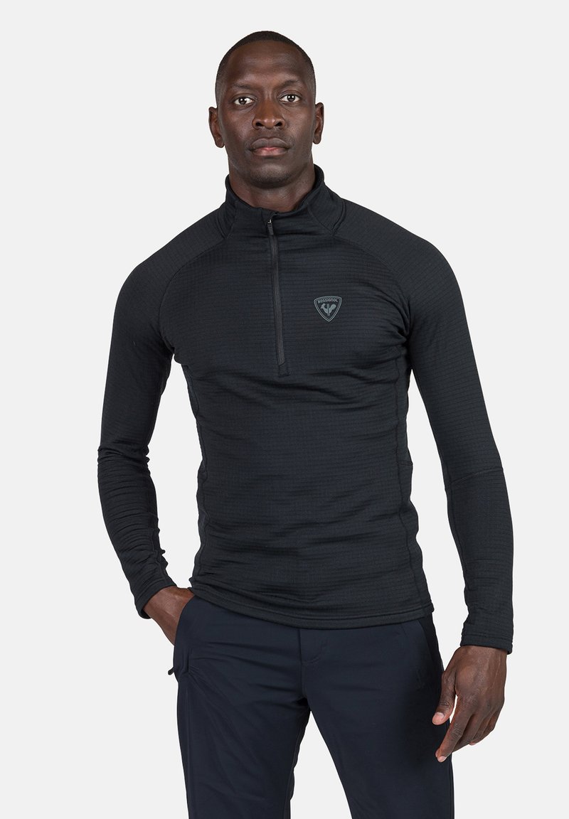 Pullover nero a maniche lunghe, con zip a quarto e motivo testurizzato, dotato di un piccolo logo sul petto. Il tessuto appare aderente e liscio.