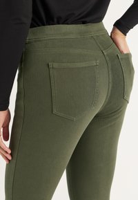 Olijfgroene stretchjeans met een hoge taille, klassieke achterzakken en subtiele stiksels. Glad textuur met een aansluitende pasvorm.