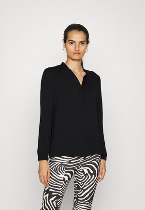 Schwarze Bluse mit langen Ärmeln und V-Ausschnitt, leicht schimmernd, kombiniert mit gemusterten schwarzen und weißen Leggings im Zebralook.