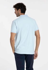 Polo shirt bleu clair à manches courtes ; comporte un col classique et un ourlet droit. Texture de tissu lisse, design minimal sans motifs.