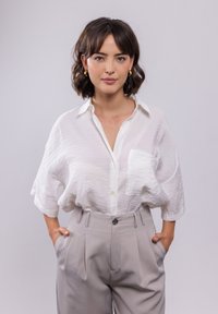 Weißes, leichtes Hemd mit Knopfverschluss und Tasche; kombiniert mit hochtaillierten, gefalteten hellgrauen Hosen. Glatter Stoff, lockere Passform.