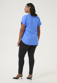 Ljusblå blus med kort ärm, slätt tyg, avslappnad passform; bärs med svarta skinny jeans och svarta slingback-hälar; enkel design.