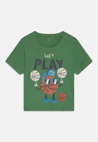 Camiseta de algodón verde con un divertido personaje de baloncesto de dibujos animados, el texto "vamos a JUGAR" y gráficos coloridos de balones de baloncesto y accesorios.