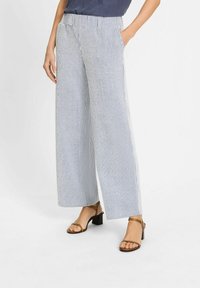 Wijdvallende broek van gestreepte stof in blauw en wit, met een elastische tailleband en zijzakken. Gepaarde met bruine sandaaltjes met banden.