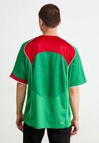 Zaļš un sarkans īsām piedurknēm sporta krekls ar punktveida rakstu, kontrastējošām krāsām un baltajiem akcentiem. Izgatavots no elpojoša sieta materiāla.