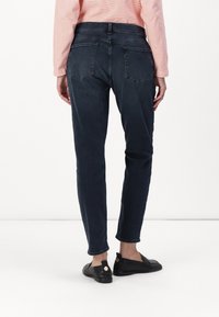 Jeans azul oscuro con corte ajustado, que cuentan con bolsillos traseros, una cintura de altura media y una textura de tejido que se asemeja al denim. Llevados con zapatos planos negros.