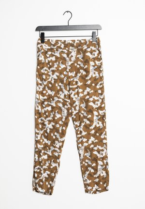 Brązowo-białe, wąskie spodnie z abstrakcyjnym wzorem wiszące na czarnym wieszaku na białym tle.