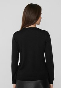 Suéter negro de manga larga, con cuello redondo y puños acanalados. Confeccionado en una tela suave, cuenta con una silueta ajustada y un diseño impecable.