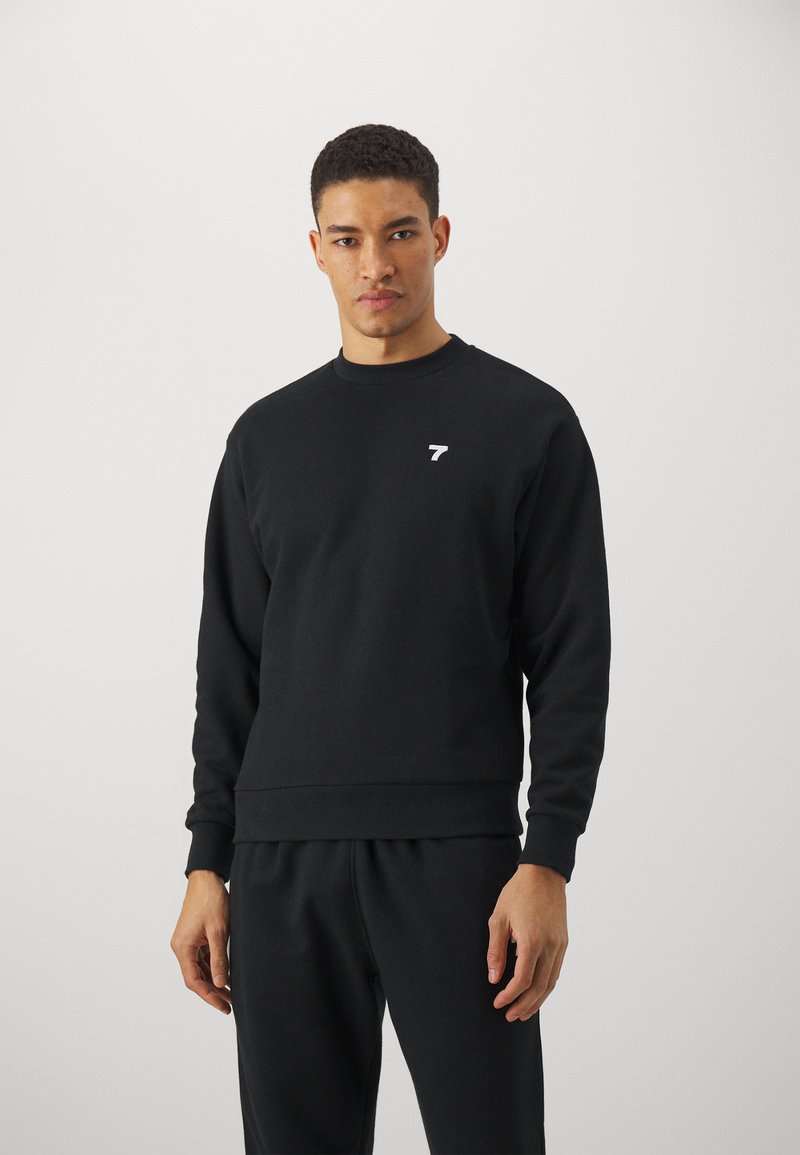 Sudadera negra hecha de una mezcla de algodón, con cuello redondo, mangas largas, puños y dobladillo acanalados, y un pequeño logo blanco en el pecho.