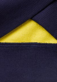 Tessuto a coste blu navy sovrapposto a maglina liscia gialla brillante, con dettagli di cucitura visibili lungo i bordi.