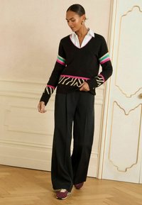 Adīta melna džemperis ar rozā un tīkkoka svītrām piedurknēs, zebras raksts apakšmalā. Saskaņots ar platām melnām biksēm un bordo sporta apaviem.