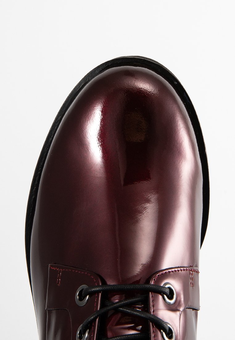 Scarpe in pelle bordeaux con finitura lucida, punta rotonda, lacci neri e dettagli di cucitura sottili. Suola in gomma nera spessa.