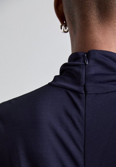 Navy high-neck garment made from smooth fabric featuring a central zipper at the back and a fitted silhouette.