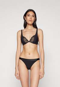Soutien-gorge noir avec des bordures en dentelle et des bretelles réglables, associé à un string noir avec une taille lisse. Les deux pièces affichent un design minimaliste.