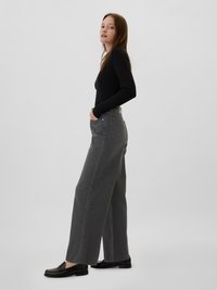 Jean large gris à taille haute, avec poches avant et texture lisse. Associé à des mocassins noirs et un haut à manches longues ajusté.