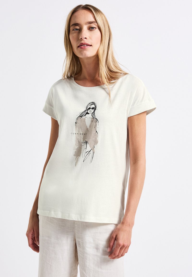 T-shirt crème à manches courtes en coton, mettant en avant un croquis minimaliste en noir d'une femme avec le mot "CONFIANT" imprimé en dessous.