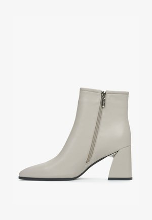 Beige leren enkelboot met een puntige neus, rits aan de zijkant en een geometrische blokhak. Glad oppervlak met minimale accenten.