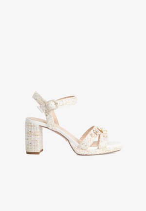 Sandale blanche en tweed à talon bloc avec bride à la cheville à boucle et perles décoratives ainsi que des ornements dorés sur les brides avant.