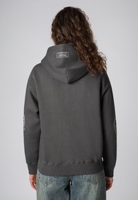Grijze hoodie met een grote kap en een label op de achterkant. Voorzien van ribgebreide manchetten en onderrand. Ontwerp bevat een grafisch motief op de linker mouw.