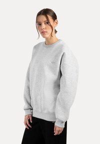 Lys grå sweatshirt lavet af blød bomuldsblanding, med rund hals, ribbede ærmer og en lille logo detalje på brystet.