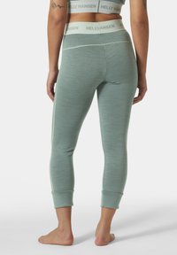 Lichtgroene leggings van rekbaar materiaal, met een fitted ontwerp, enkelmanchetten en een elastische tailleband met "HELLY HANSEN" branding.