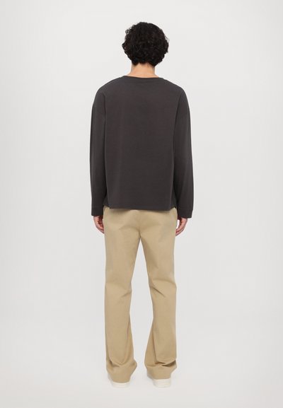 Langarmig shirt in antracietgrijs met een relaxte pasvorm, gecombineerd met lichte beige broeken. Eenvoudig ontwerp, zachte stof, standaard ronde halslijn.