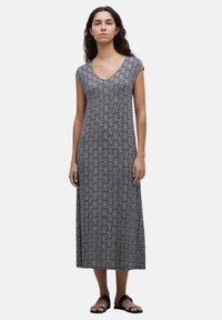 Vestido maxi negro y blanco con un patrón, escote en V, mangas cortas y un corte relajado, confeccionado en una tela suave. Sandalias planas completan el conjunto.