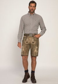 Braun kariertes Button-Up-Hemd, knielange braune Lederhosen mit dekorativer Stickerei, silberne Gürtelschnalle, dunkle Socken und braune Schnürstiefel.
