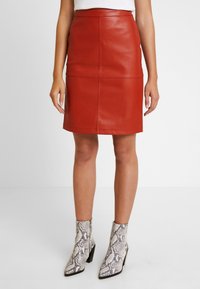 Červená kožená tužková sukně s těsným střihem, obsahující švy a hladkou texturu, doplněná o vzorované kotníkové boty.