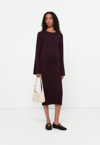 Abito bordò a maniche lunghe con coste e spacco laterale; abbinato a una borsa crema e scarpe slip-on nere con borchie.