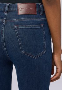 Mörkblå denimjeans med en läderpatch från Trussardi på midjan, kontrasterande röd sömnad och en enkel bakfickedesign.