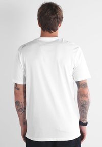 T-shirt blanc à manches courtes avec col rond, texture lisse, couture d'épaule renforcée et une étiquette logo sur la partie supérieure du dos.