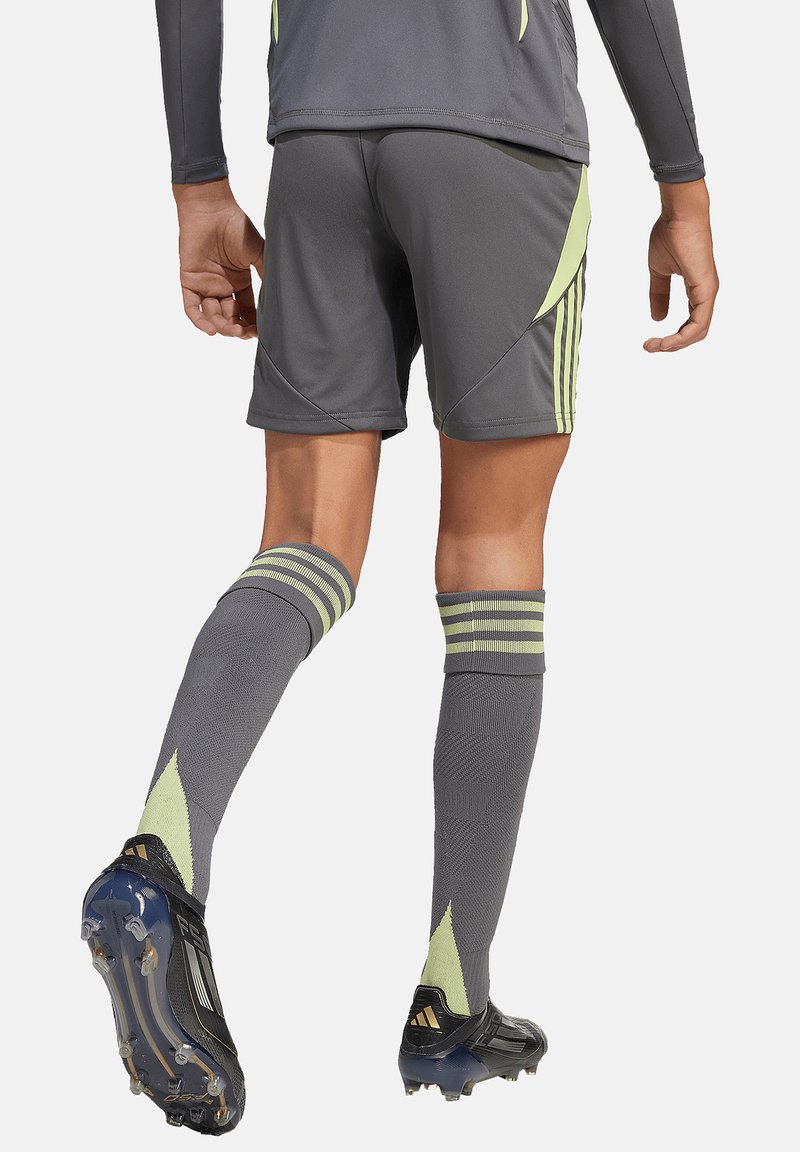 Personne portant un short de football gris et jaune, des chaussettes hautes assorties et des crampons noirs, debout, de dos face à l'appareil photo.