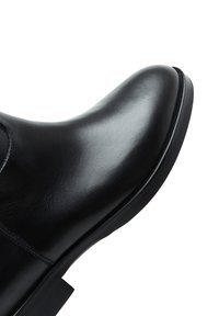 Bottine en cuir noir avec un bout arrondi, surface lisse, couture discrète et semelle en caoutchouc noir. Design minimaliste, style classique.