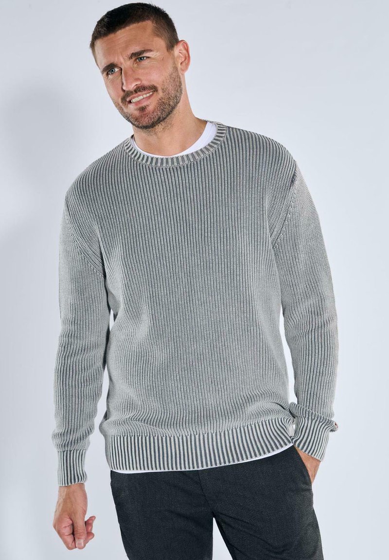 Grauer gerippter Pullover mit runder Halslinie, langen Ärmeln und gestreiften Bündchen. Über einem weißen Hemd getragen, das ein strukturiertes Strickdesign aufweist.