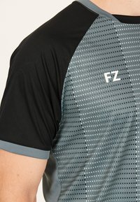 Grå och svart idrottströja med korta ärmar, försedd med prickiga mönster och "FZ"-logotypen i vitt på bröstet. Slät tygstruktur.