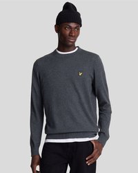 Pull en tricot gris foncé avec un col rond, des poignets et un ourlet à côtes. Présente un petit logo jaune sur la poitrine. Porté par-dessus une chemise blanche.