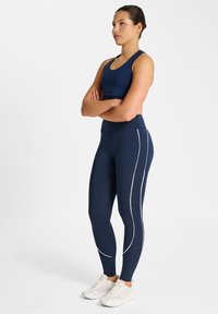 Marinblå sport-bh och leggings med vit sidolinje, gjorda av stretchigt tyg; kombinerade med ljusa sportskor.