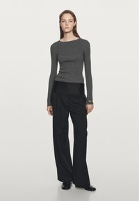 Grijze lange mouwtop met een slim fit ontwerp, gecombineerd met losse zwarte broek met een soepele tailleband. Het model staat tegen een effen achtergrond.