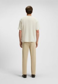 Camicia corta beige chiaro a maniche corte con una vestibilità rilassata, abbinata a pantaloni beige chiaro. Tessuto liscio, design minimal e senza motivi visibili.