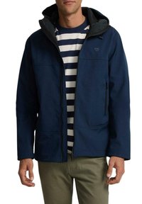 Chaqueta azul marino con capucha, con cierre frontal de cremallera, dos bolsillos frontales y una textura suave, llevada sobre una camisa a rayas.