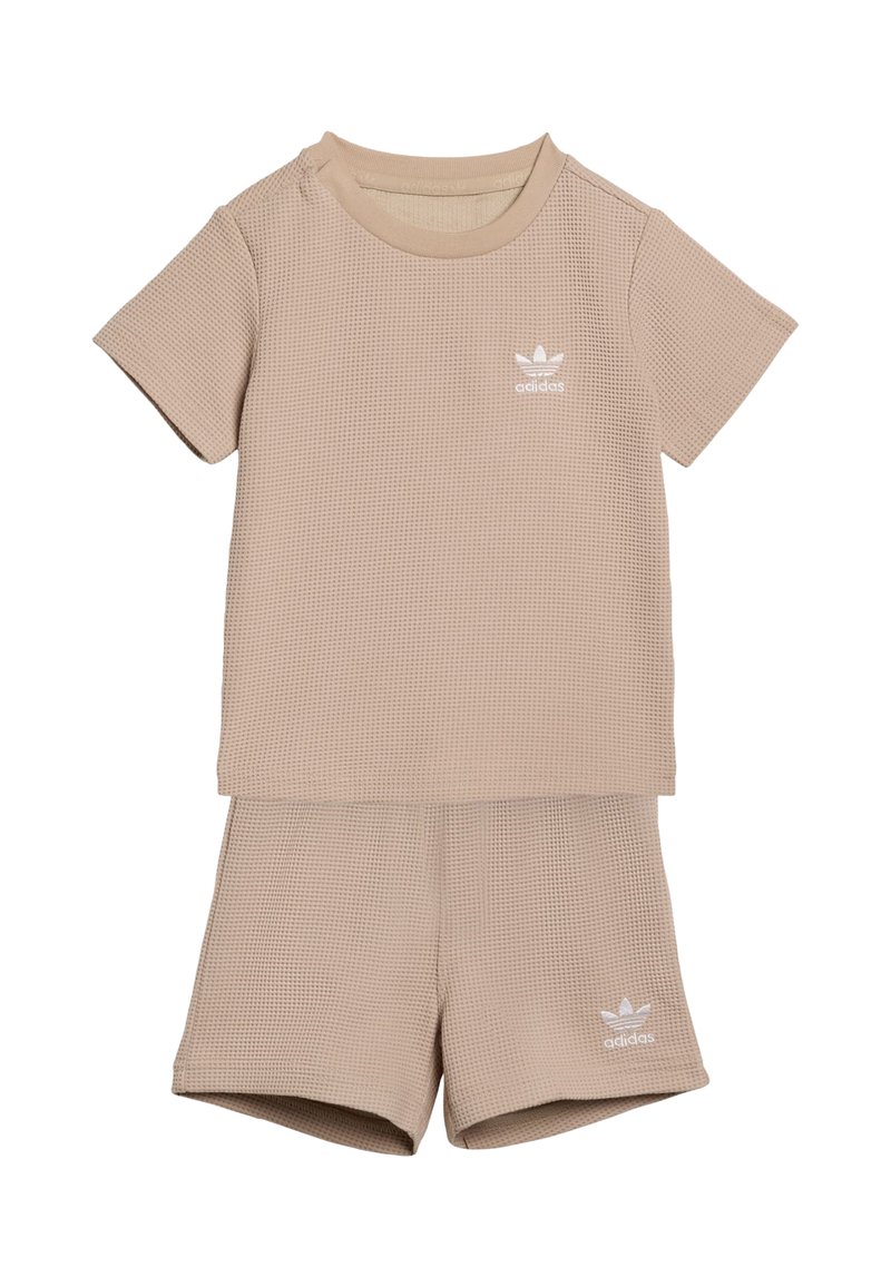 Conjunto beige de dos piezas que incluye una camiseta de manga corta y textura, y pantalones cortos a juego, ambos con un pequeño logo blanco de adidas.