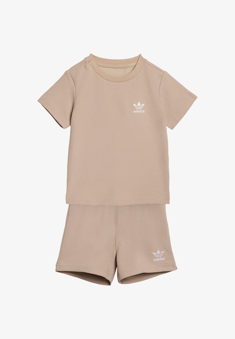 Conjunto beige de dos piezas que incluye una camiseta de manga corta y textura, y pantalones cortos a juego, ambos con un pequeño logo blanco de adidas.