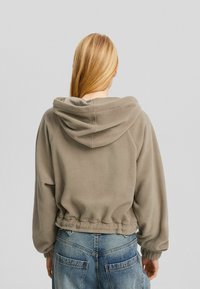 Harmaa fleecetakki hupulla, joustavilla hihansuuilla ja lyhennetty malli, yhdistetty korkeavyötäröisiin sinisiin farkkuihin.